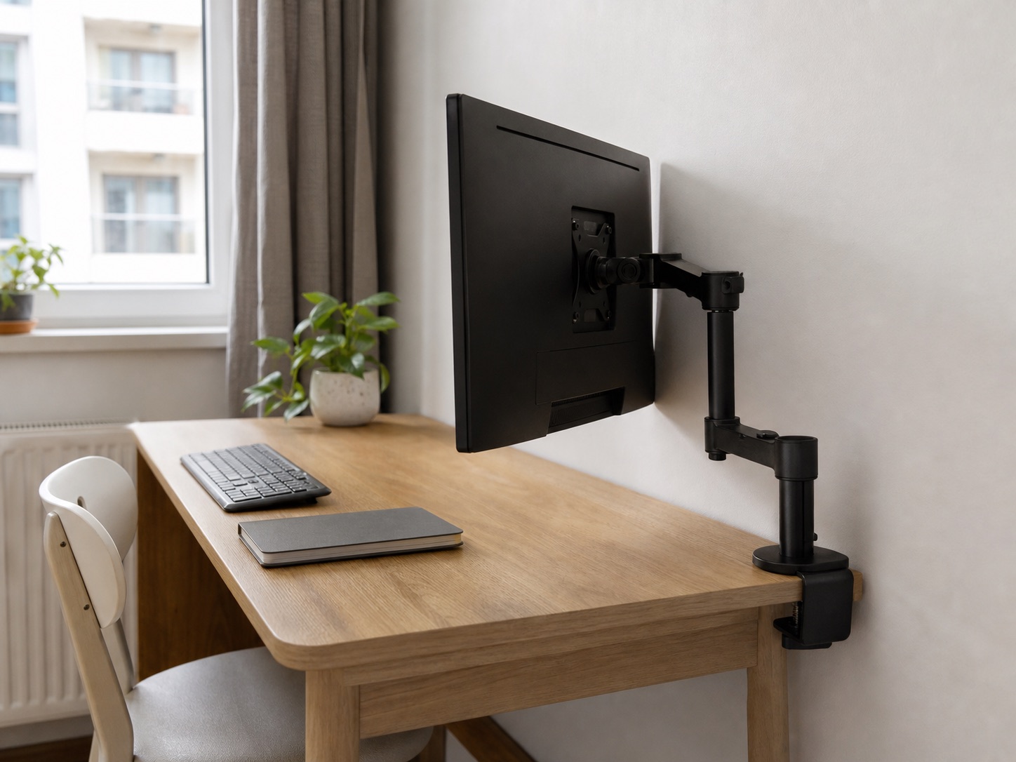 Single monitor arm folded beside a screen on a shallow desk close to a wall